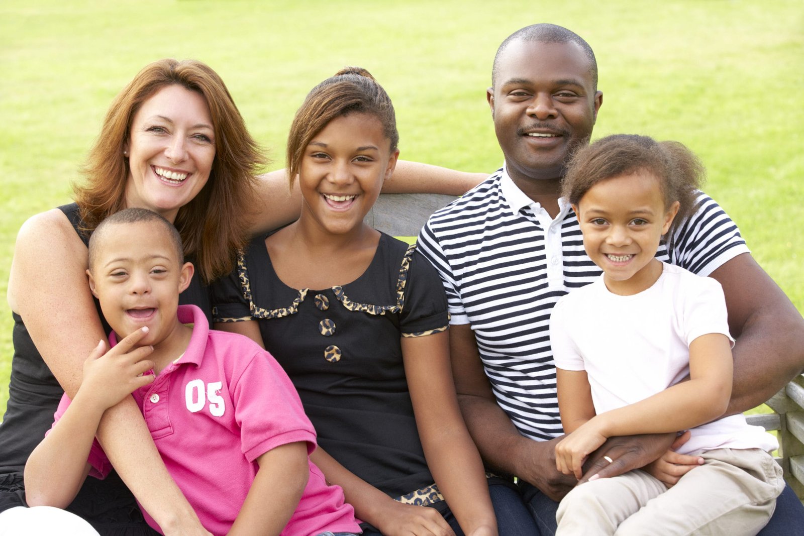 A family all smiling at the camera, one of the children has down syndrome.