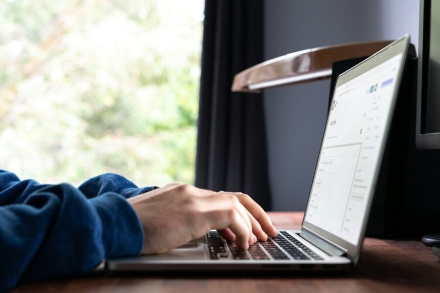 Person typing on a laptop at a wooden desk, with the screen displaying the “Simple Author Box Pro” website. A smartphone, books, and small desk items are also visible nearby.