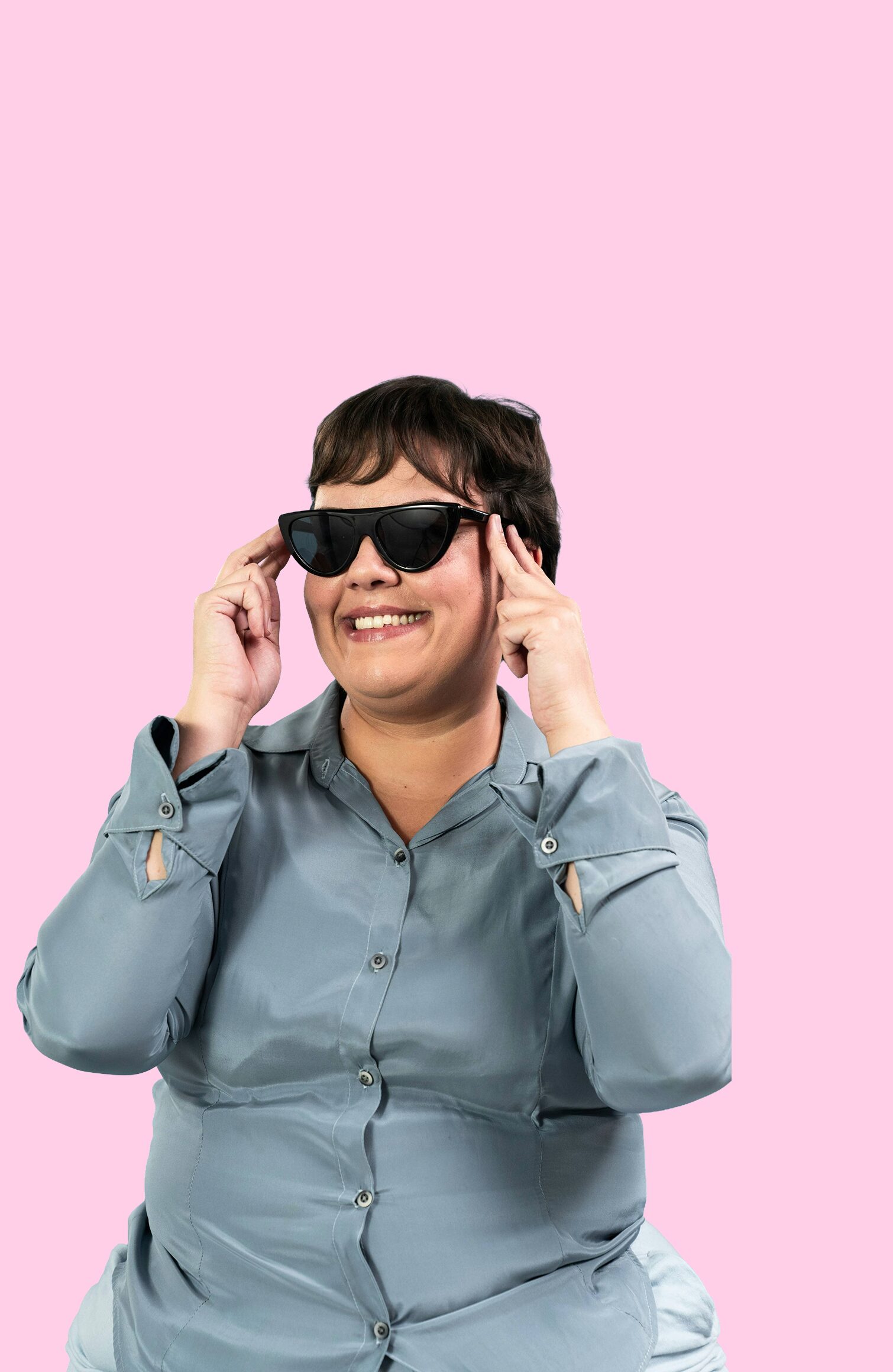A smiling woman wearing sunglasses and a light blue shirt, set against a pink background.