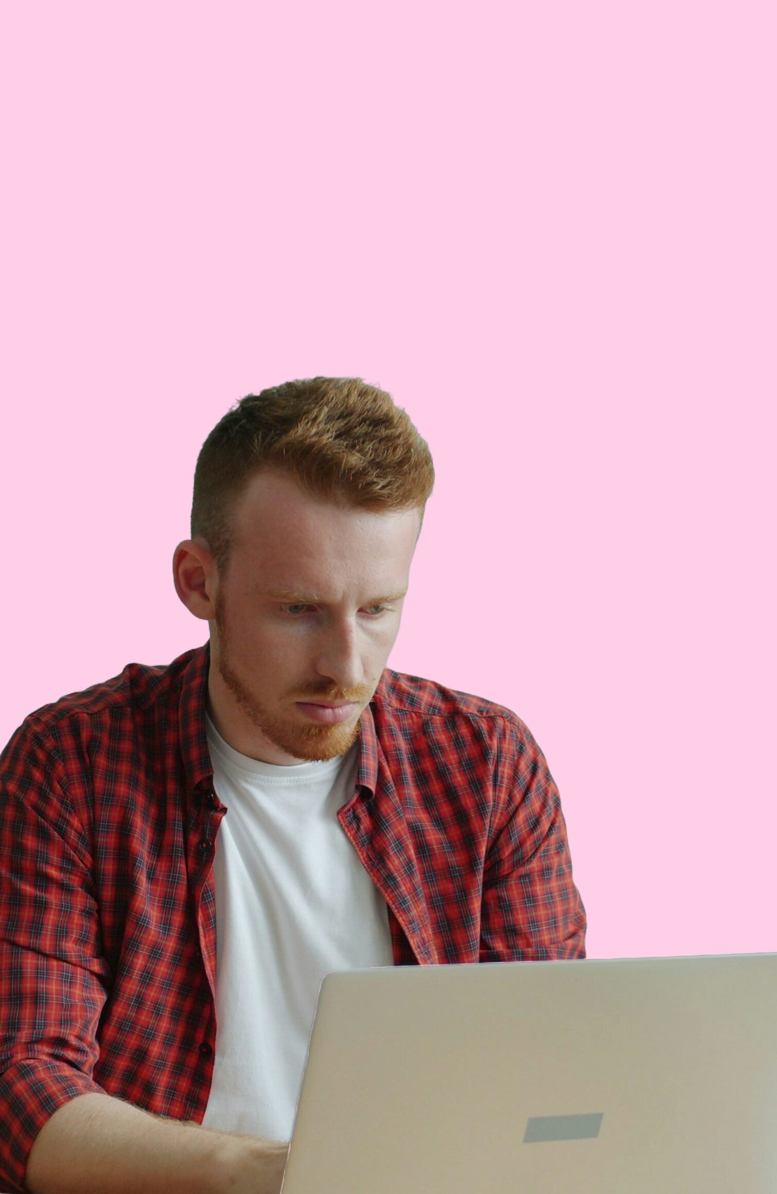 man sitting at a desk and working on a laptop, with a pink background.