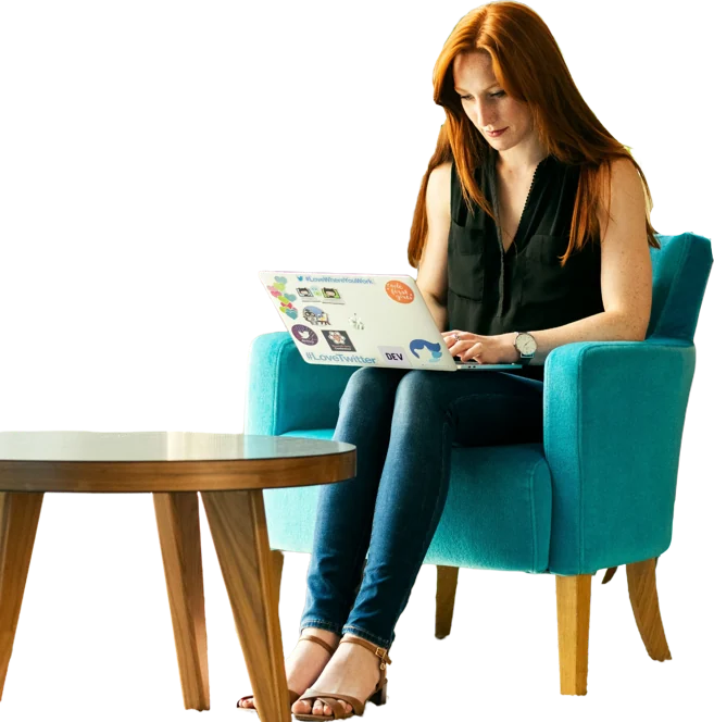 Woman with red hair working on a laptop in a teal armchair